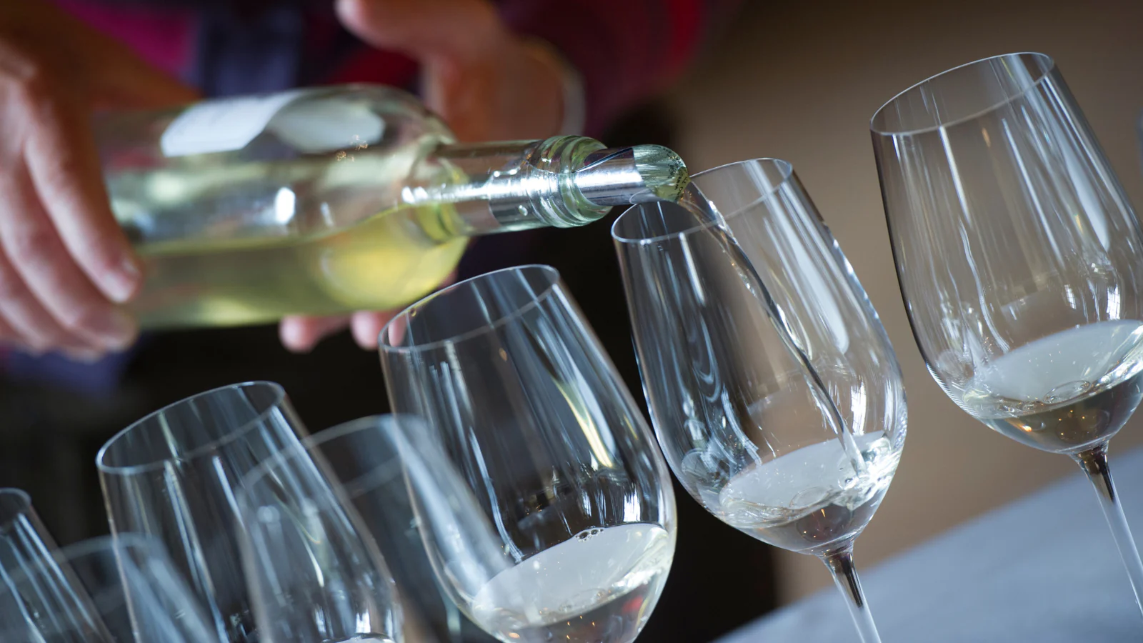 En människa som häller upp vin i ett av flera vinglas